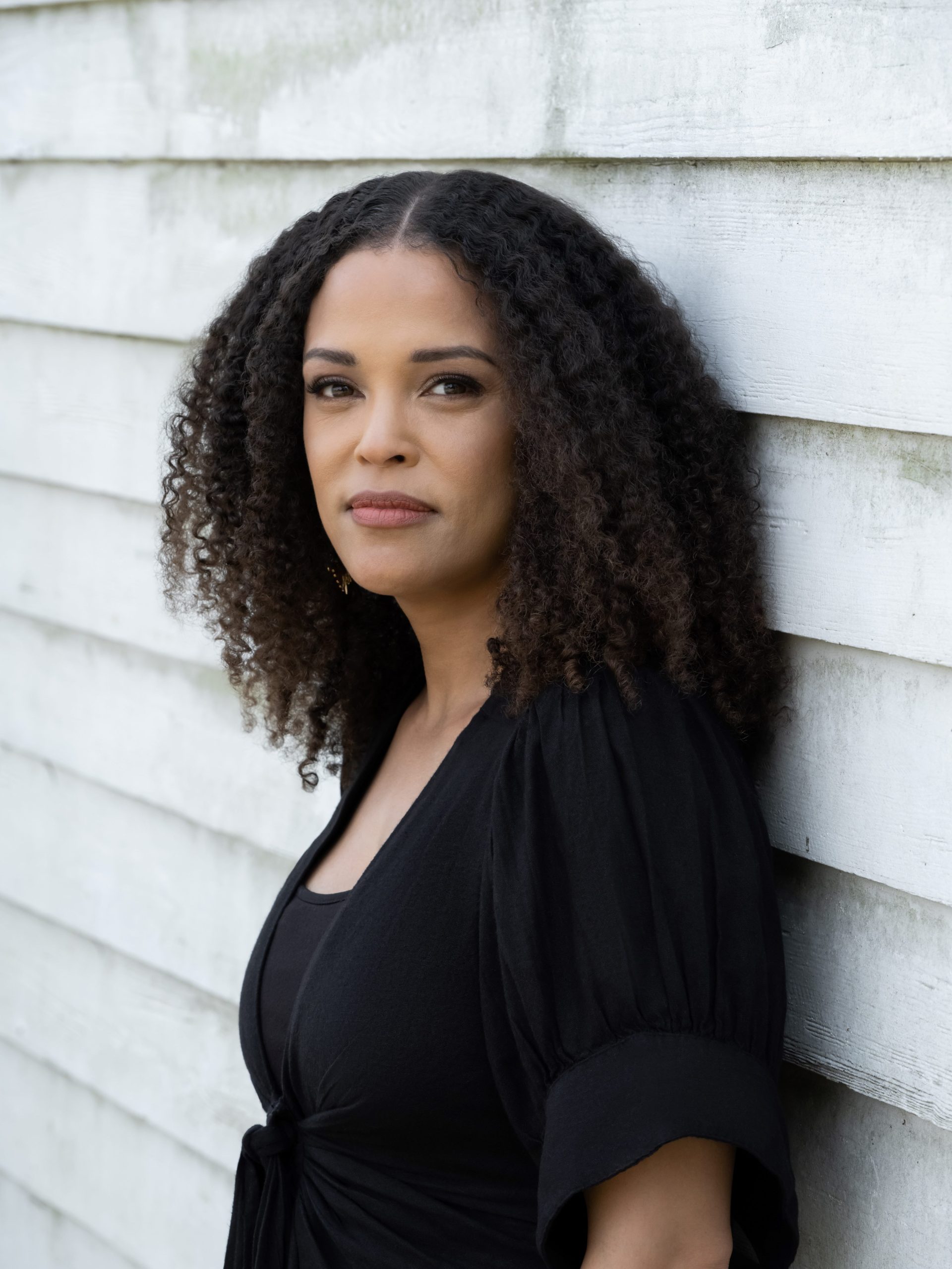 Jesmyn Ward looks at the camera against a white barn with shiplap siding
